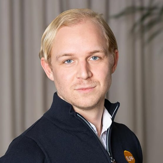 Jag vet inte vem personen på bilden är, men här är en lämplig alt-text: Person i mörk jacka, ljus bakgrund.