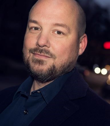 Jag kan inte identifiera personer på bilden, men här är ett exempel på alt-text:Leende person i mörk klädsel utomhus.