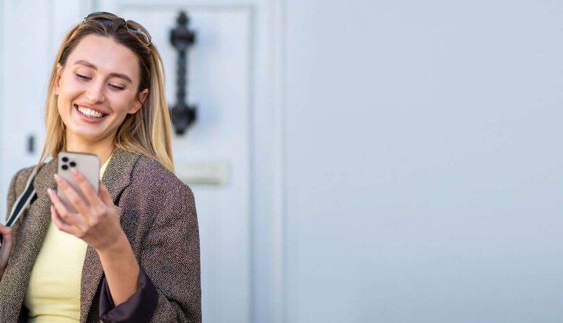 Leende kvinna som tittar på sin mobiltelefon.