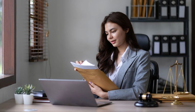 Kvinna vid skrivbord med dokument, dator och rättssymboler.